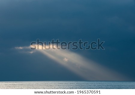 Gorgeous sunbeam coming out from behind the dark clouds illuminating the serene ocean, reminds us of heaven and God. Natural blue background. Iriomote Island. Royalty-Free Stock Photo #1965370591