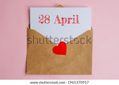 Kraft envelope with a white sheet of paper and a date 28 april, with red heart. Flat lay on pink background, romance and love concept