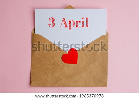Kraft envelope with a white sheet of paper and a date 3 april, with red heart. Flat lay on pink background, romance and love concept