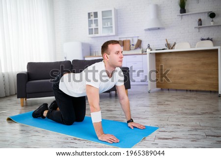 Young man sitting on carpet in his home and doing stretching after sports