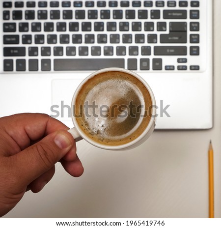  Top view of male hand with  coffee cup above laptop. empty brown notebook with yellow pencil. 