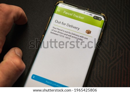 Male thumb finger over parcel delivery app on smartphone screen.