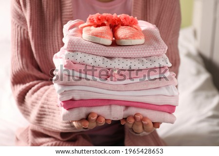 Woman holding stack of baby girl's clothes with shoes indoors, closeup