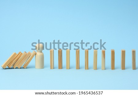 wooden model of a man stops falling of wooden bars on a light blue background. The concept of a strong and courageous personality capable of withstanding unequal difficulties Royalty-Free Stock Photo #1965436537