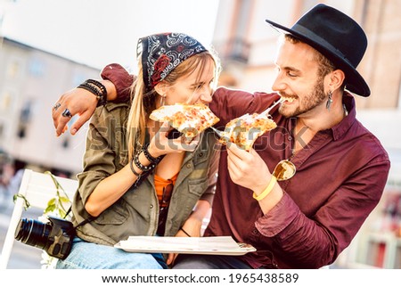 Young hipster couple eating pizza at bar restaurant outdoors - Happy relationship concept with millenial boyfriend and girlfriend having fun moments together - Bright vivid filter with focus on faces Royalty-Free Stock Photo #1965438589