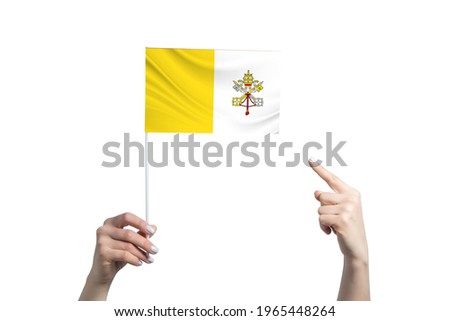 A beautiful female hand holds a Vatican flag to which she shows the finger of her other hand, isolated on white background.