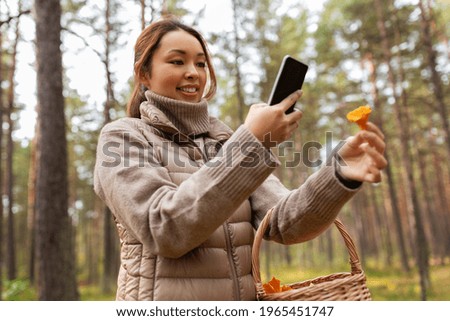 technology, leisure and people concept - young asian woman with smartphone using app to identify mushroom in autumn forest