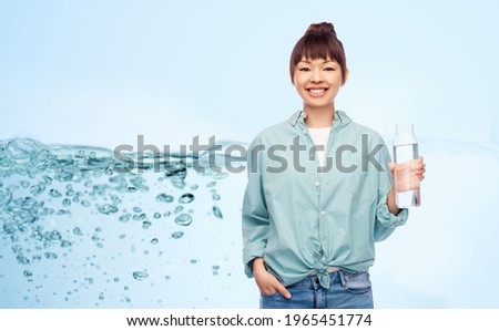 people concept - portrait of young asian woman in turquoise shirt holding reusable glass bottle with water over blue background with bubbles in water splash
