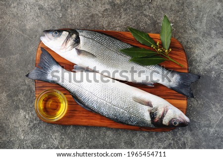Fresh raw sea bass on a cutting board with olive oil and laurel leaf. Royalty-Free Stock Photo #1965454711