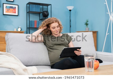 Young Pregnant woman using tablet search pregnancy information. Mom feeling happy smiling positive and peaceful while take care her child lying on sofa in living room at home concept.