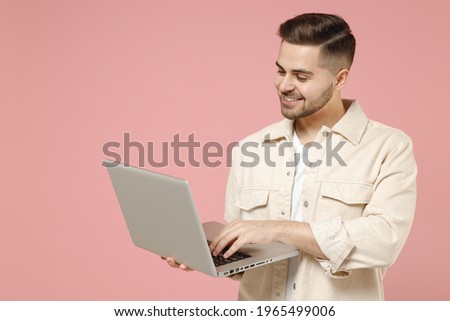 Young copywriter happy freelancer caucasian man 20s wearing jacket white t-shirt using laptop pc computer chatting in social network online isolated on pastel pink color background studio portrait. Royalty-Free Stock Photo #1965499006