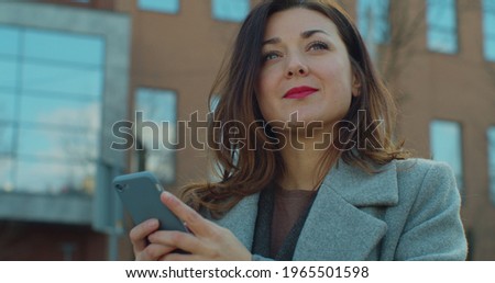 Close up smiling successful businesswoman use smartphone near business center. Young pretty woman using social networks, typing messages outdoor.