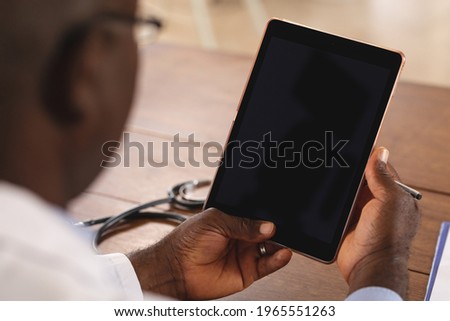 Mid section of african american senior male doctor holding digital tablet with copy space at home. distant communication and telemedicine consultation concept.
