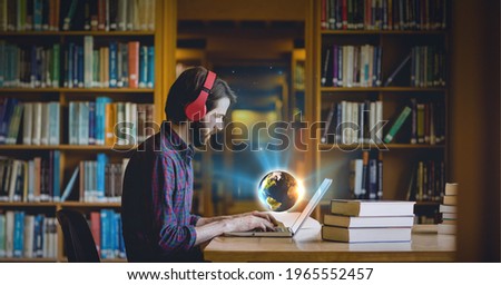 Composition of glowing globe over man wearing headphones in library using laptop. global technology, data processing and digital interface concept digitally generated image.