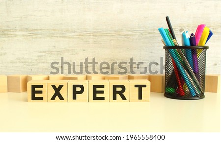 Six stacked wooden cubes with letters EXPERT on a white work table on a gray background. Business concept