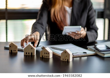 Close up wooden toy house with business woman signs a purchase contract or mortgage for a home, Real estate concept.	