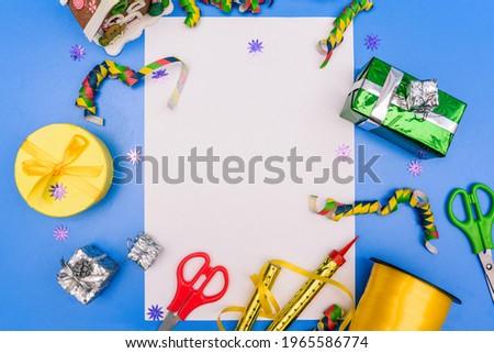 Postcard for the holiday. Birthday background. Table with gifts, scissors and a festive whistle. White sheet of paper for text. Top view, flat lay.