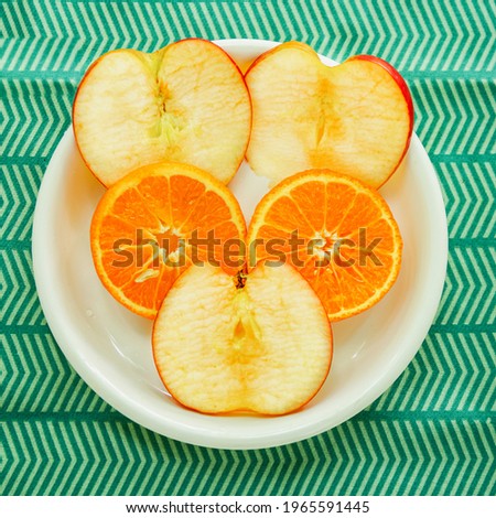 Slices of apple and orange are laid out on a plate in the form of a rabbit's face.