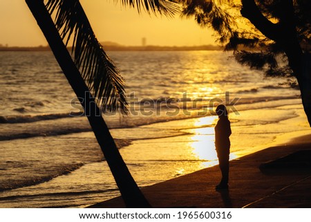 Silhouette picture of woman standing on beach with the sea and sunset at Suan Son Beach, Rayong, Thailand.