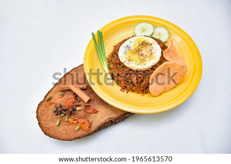 Nasi goreng fried rice with shrimps and egg bulsai garnished with fresh cucumber slices and prawn crackers on a yellow plate on white background with a wood slide. Asian food Indian, masala