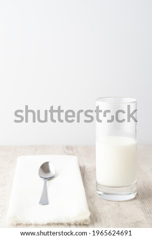 Glass of milk with metal spoon on white napkin on wooden table. High key