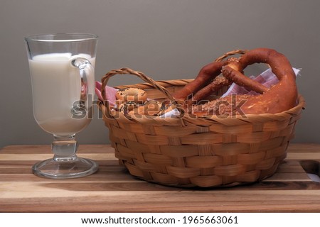 a glass glass of milk sits on the cutting board next to a basket of buns and dried poppies.