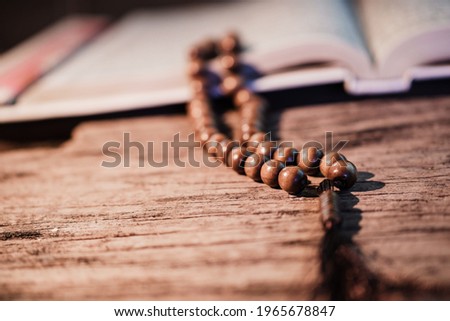 Islamic prayer beads or tasbih on the Quran on a rustic wooden surface. It is suitable for the background of Ramadan-themed design concepts or other Islamic religious events.