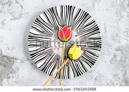 two gingerbread flowers and small hearts on white and black plate on marble background