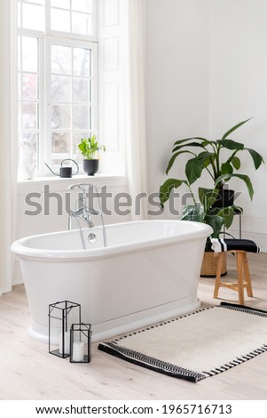 Stylish modern bathroom interior. Vertical view of empty freestanding bathtub on wooden floor in middle light room against large window and green houseplants Royalty-Free Stock Photo #1965716713
