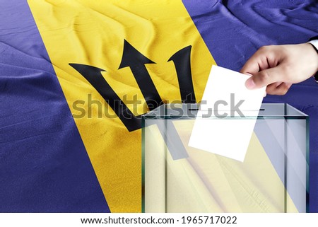 barbados flag, barbados  the symbol of elections Male hand puts down a white sheet of paper with a mark as a symbol of a ballot paper against the background of the 
