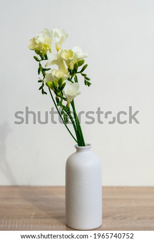 Portrait white picture frame mockup on wooden table. Modern ceramic vase with yelow freesia flowers . White wall background. Scandinavian interior. 