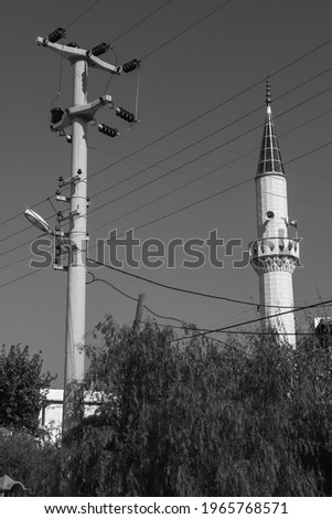 electric pole and many electric wires, mosque minaret in the background (black and white photo)