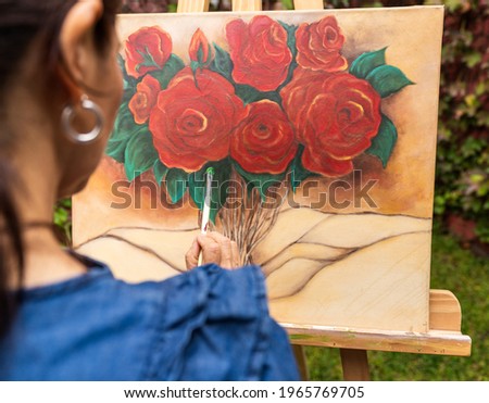woman painting a picture on a frame on a wooden lectern outdoors