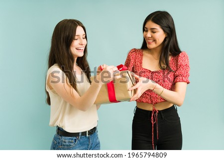 Latin young woman giving her cheerful best friend a surprise present. Pretty caucasian woman opening a gift from a friend