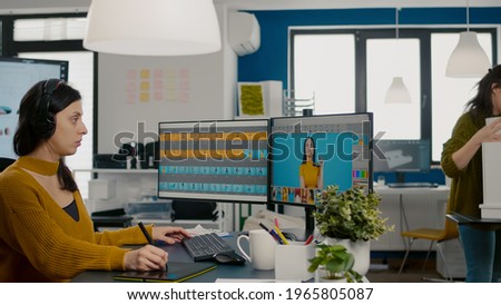 Focused retoucher specialist working at computer in creative office environment wearing headset. Color designer editing fashion photograph in digital graphics editing software with stylus pencil