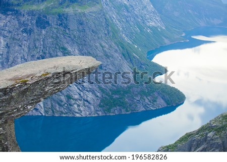 A vibrant picture of famous norwegian hiking place - trolltunga, the trolls tongue, rock skjegedall, with a tourist, and lake ringedalsvatnet and mountain panoramic scenery epic view, Norway 