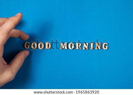 Good morning text made from wooden letters on blue background. The hand putting the first letter. Concept photo of the start of a new good day.