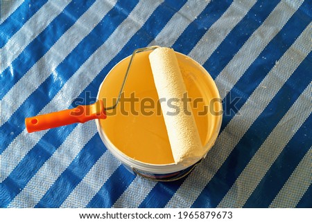 There is a bucket of yellow paint and a roller on the floor. 

