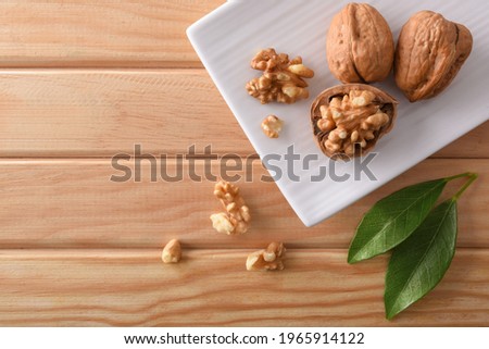 Detail walnuts with the broken shell revealing the seed on white plate on wooden table and leaves. Top view.