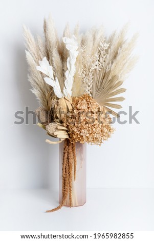 Dried flower arrangement in a pink vase. Including Banksia, Hydrangea, pampas grass, Palm Fronds, cream Ruscus leaves, and rust Amaranthus. Photographed on a white background.