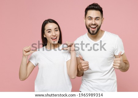 Young cheerful couple two friends bearded man brunette woman in white basic blank print design t-shirts smiling showing thumbs up like gesture isolated on pastel pink color background studio portrait Royalty-Free Stock Photo #1965989314