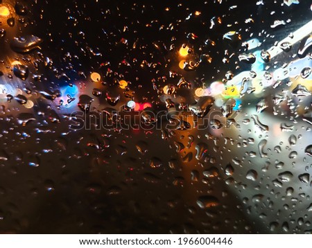 Raindrops on the car window in the night city against the background of glowing signs of shops and passing cars