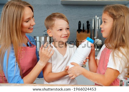 Cute blonde kids helping their mom at kitchen passing bottle of milk