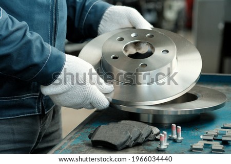 Brake disc in the hands of a mechanic close-up. On the desktop is a set of brake pads.Spare parts of the car suspension. Repair and maintenance of the car in the service center. Royalty-Free Stock Photo #1966034440