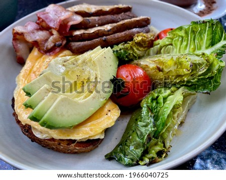 Healthy american breakfast. Eggs served with grilled salad, bread, bacon and mushrooms. This picture focuses on avocado. 
