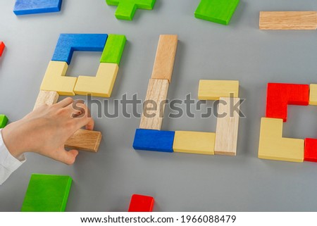 Boy's hand with a wooden cube on the gray background. Multi-colored cubes on the table. Geometric shapes on a wooden background. Puzzle concept. High quality photo