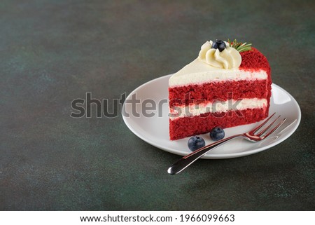 Red Velvet cake with blueberries on white plate over dark green background. Copy space.