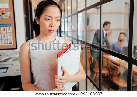 Sad pensive young businesswoman with documents folders passing by meeting room