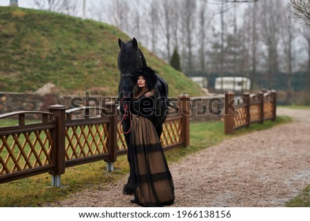 A girl in a vintage dress walks with her horse, a girl in a black fur hat, delicate makeup. Art photo