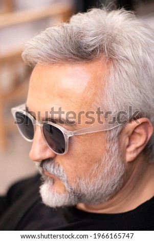 Close up portrait of handsome bearded and grey hair man wearing stylish white eyeglasses looking away on the street. Vertically photo